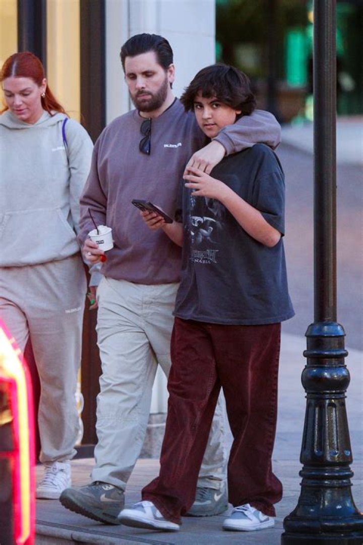 Kourtney Kardashian Rocks A White Bodysuit & Tan Trousers With A Scott Disick Look-Alike